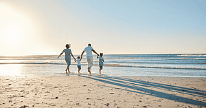 Family running on beach in the sunlight hands locked running towards ocean