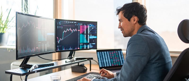 Man in suit looking at computer monitor screen of stock market in daylight