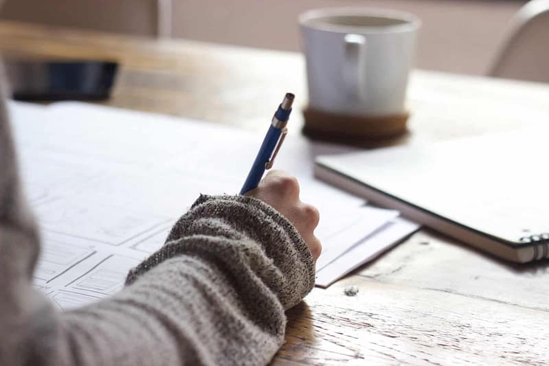 Women writing with pen on document while drinking coffee