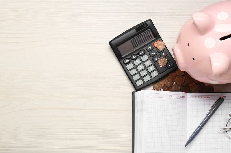 alculator, piggy bank, notebook and coins on white wooden table, flat lay. Space for text